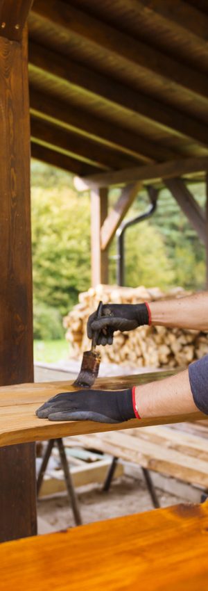 Handyman varnishing pine wooden planks in patio outside the new house